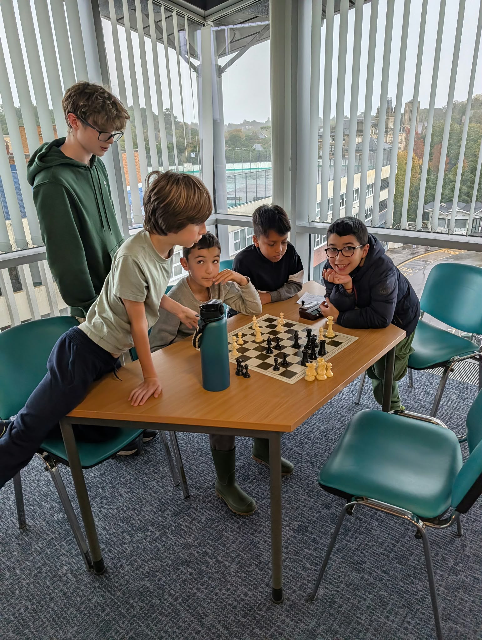 Four boys playing chess at two boards near the window